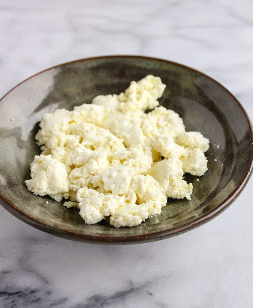 A bowl of homemade ricotta cheese with fresh herbs