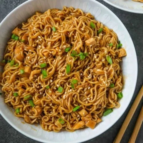 Bowl of quick saucy ramen noodles topped with scallions and sesame seeds.