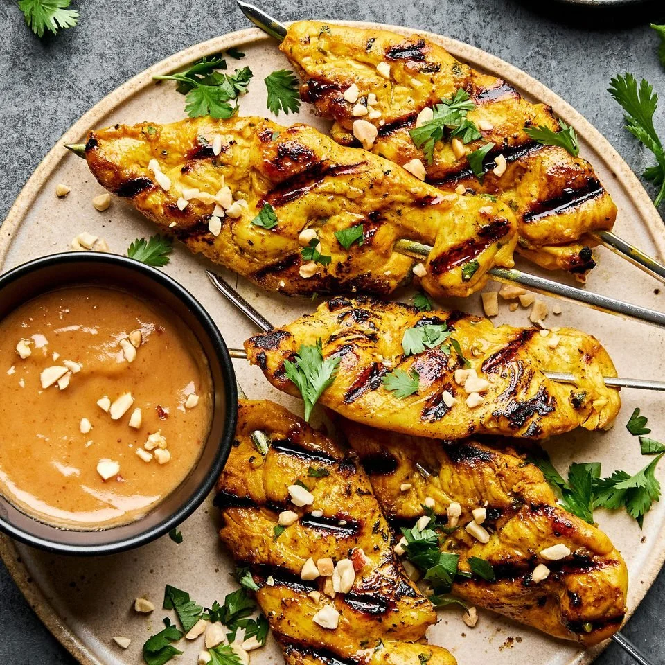 Plate of satay chicken skewers with peanut sauce and vegetables